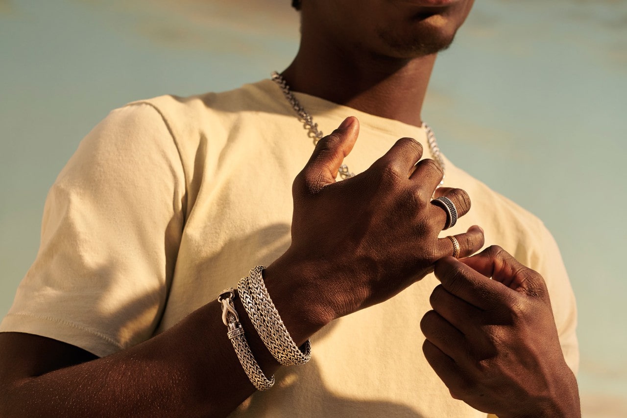 A man wearing silver John Hardy bracelets, rings, and a necklace