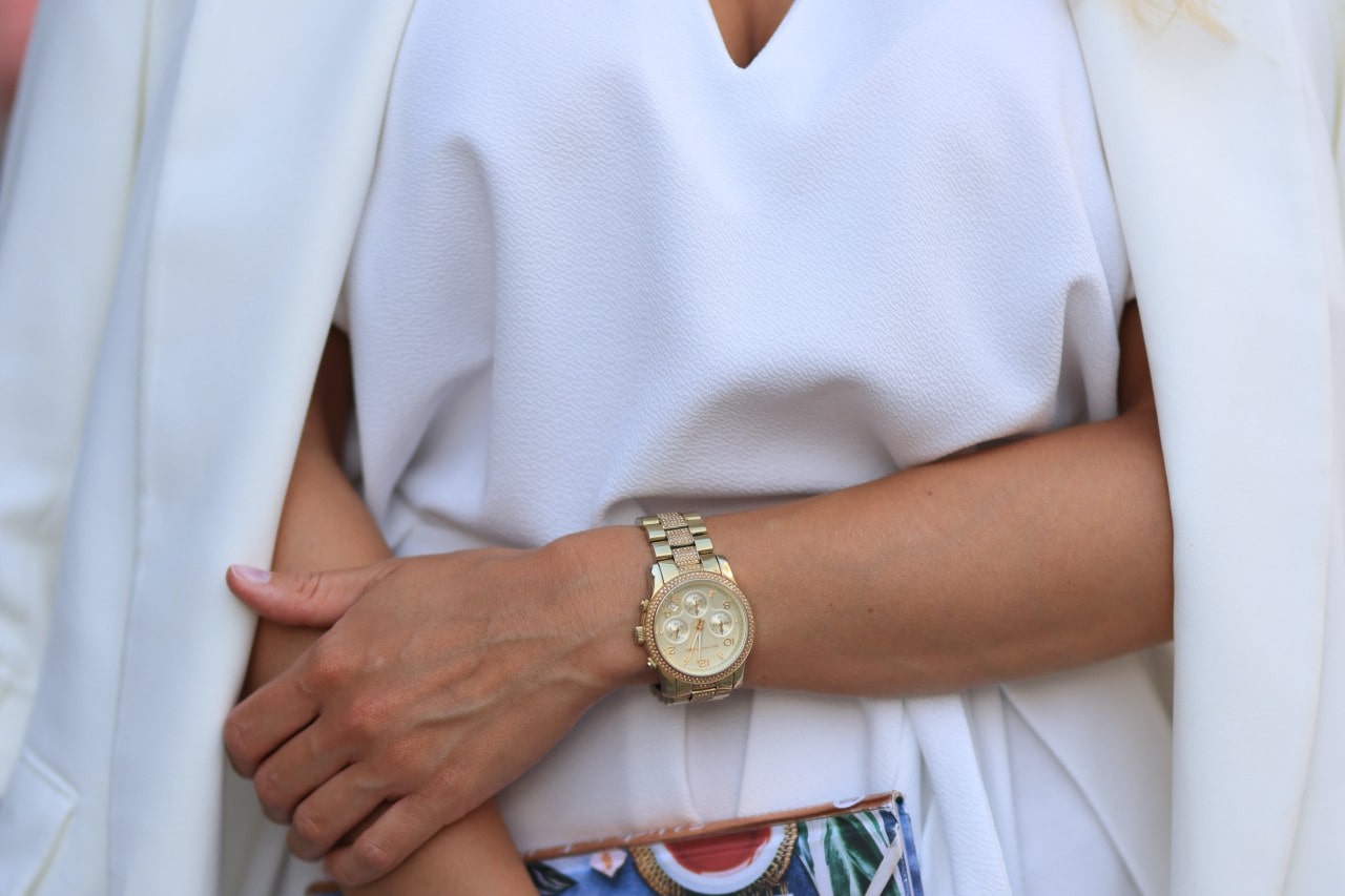 A close up of a woman in white attire, showcasing a gold plated wristwatch.