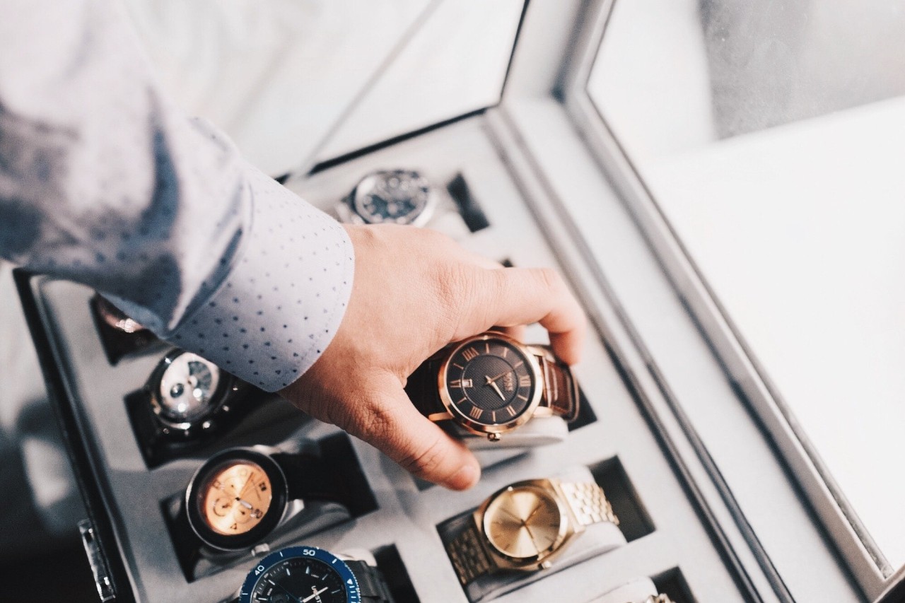 A hand in a dotted shirt picks a watch from a big watch winder.