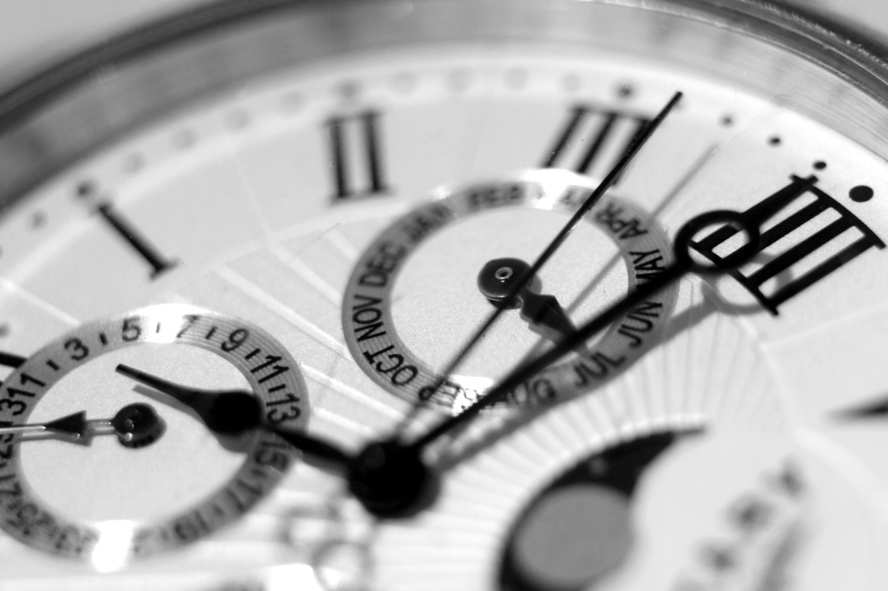 A black and white photo of a close up of a watches dial with roman numerals and several subdials.