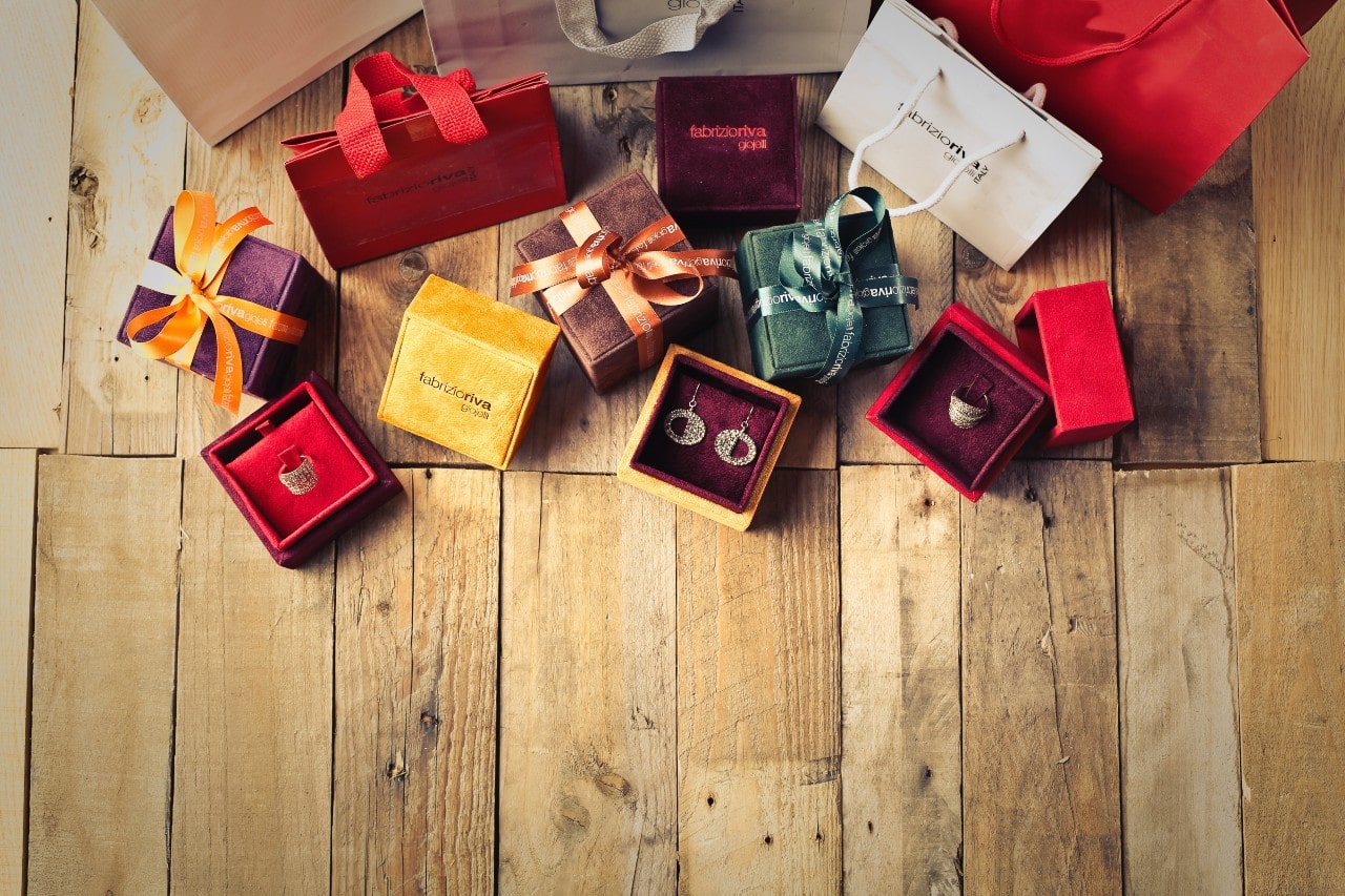 Several velvet jewelry boxes with ribbons scattered around the wooden floor, showcasing earrings and rings.