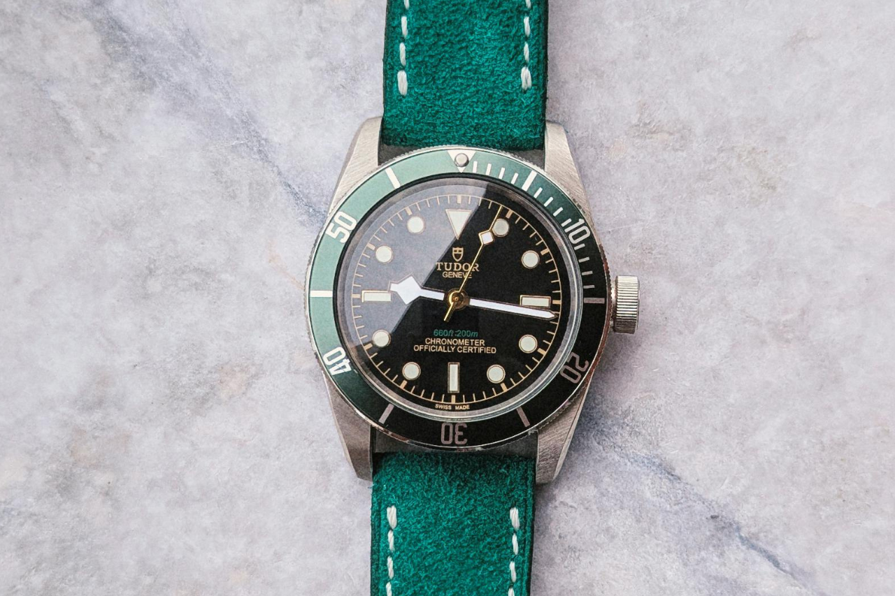 A TUDOR watch with a black dial, green bezel, and green bracelet on a marble surface.