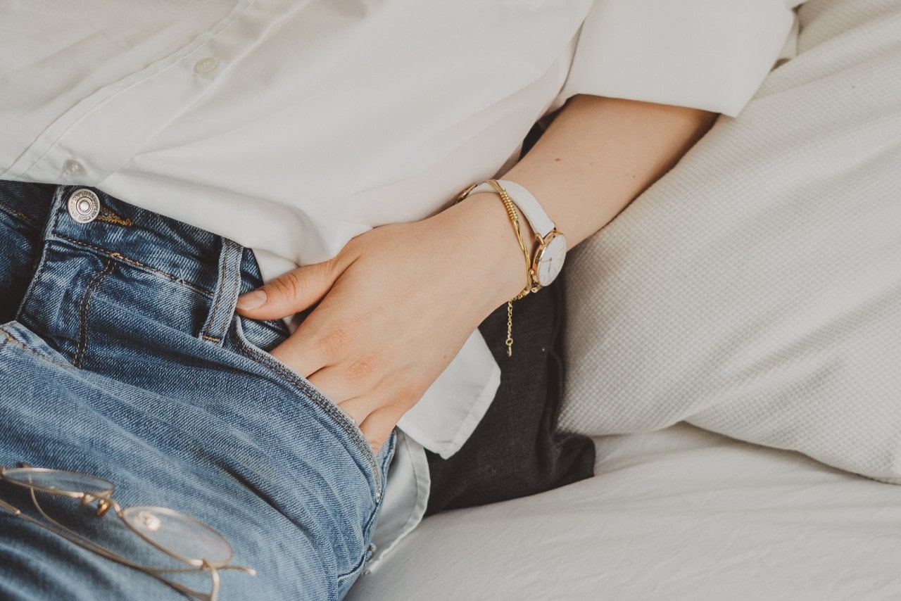 close up image of a woman’s hand in her pocket wearing a white shirt and white watch