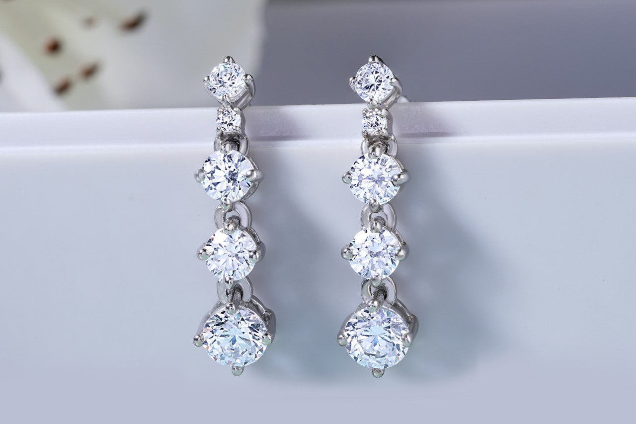 A pair of drop diamond earrings on a white surface.