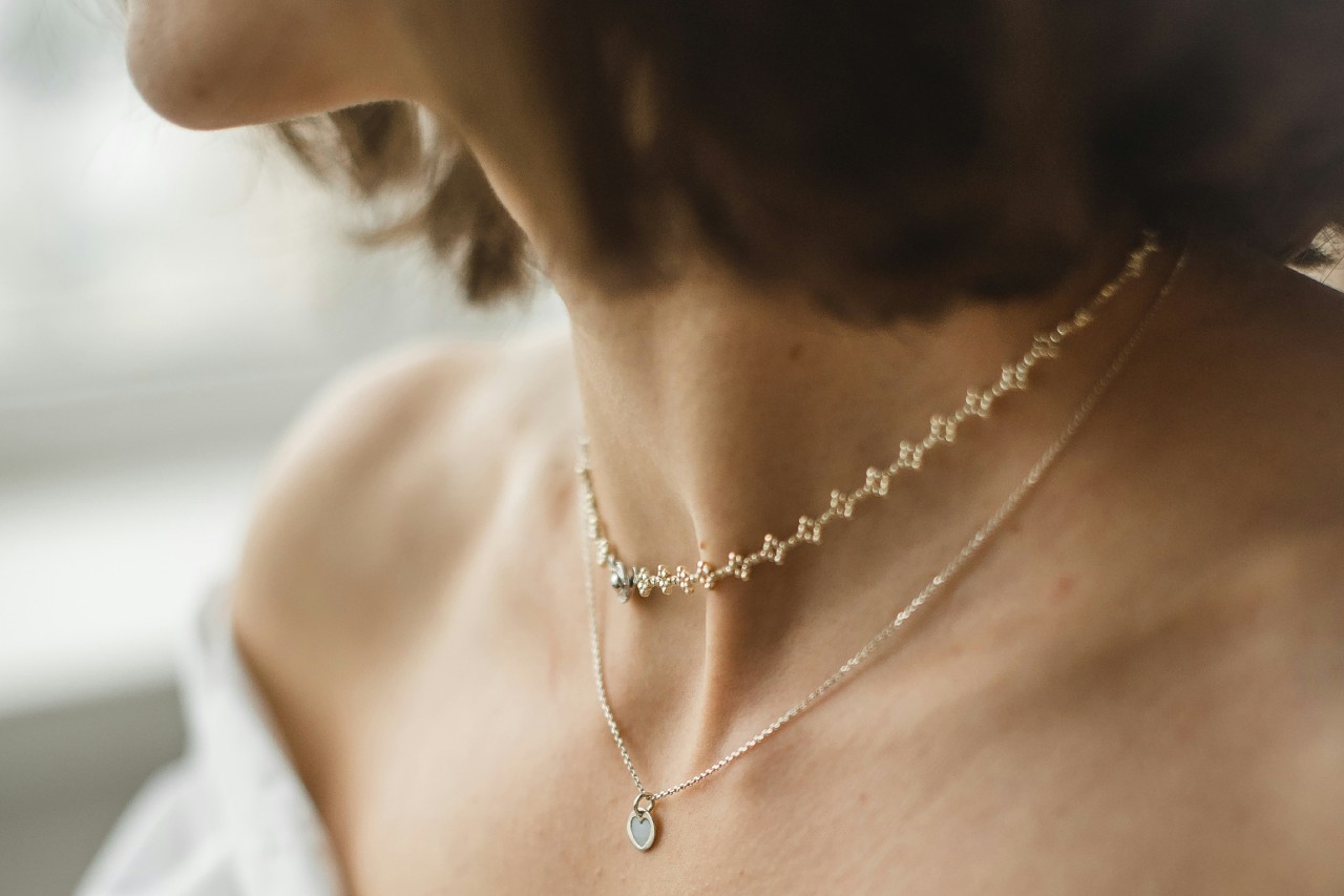 A close up of a woman’s neck in a shoulder-less top, showcasing layered yellow gold necklace.