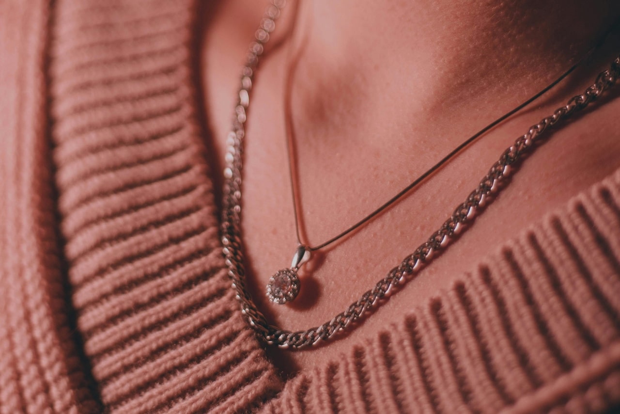 A close up of a woman's neck in a v-neck sweater, showcasing a white gold pendant and chain necklace.