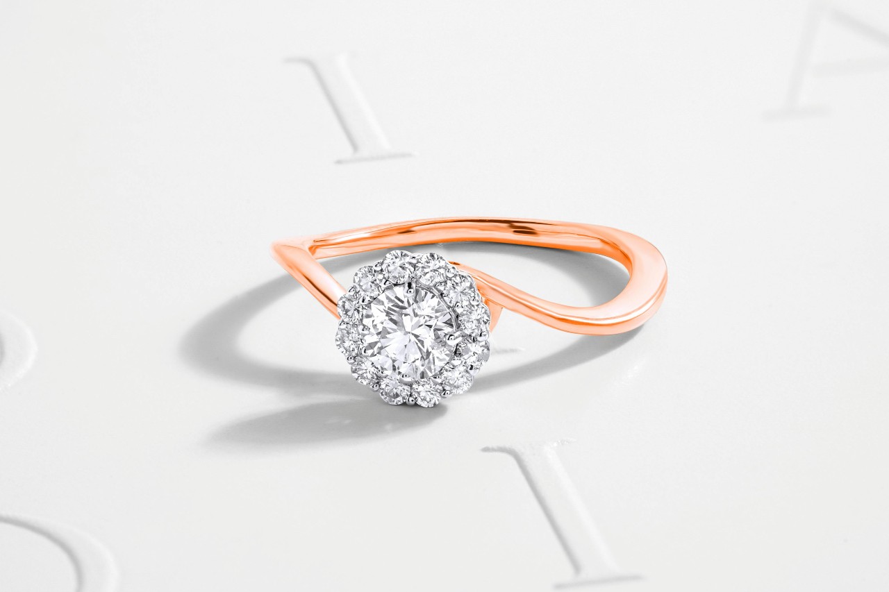 A rose gold ring with a halo of small diamonds encircling a larger central diamond.