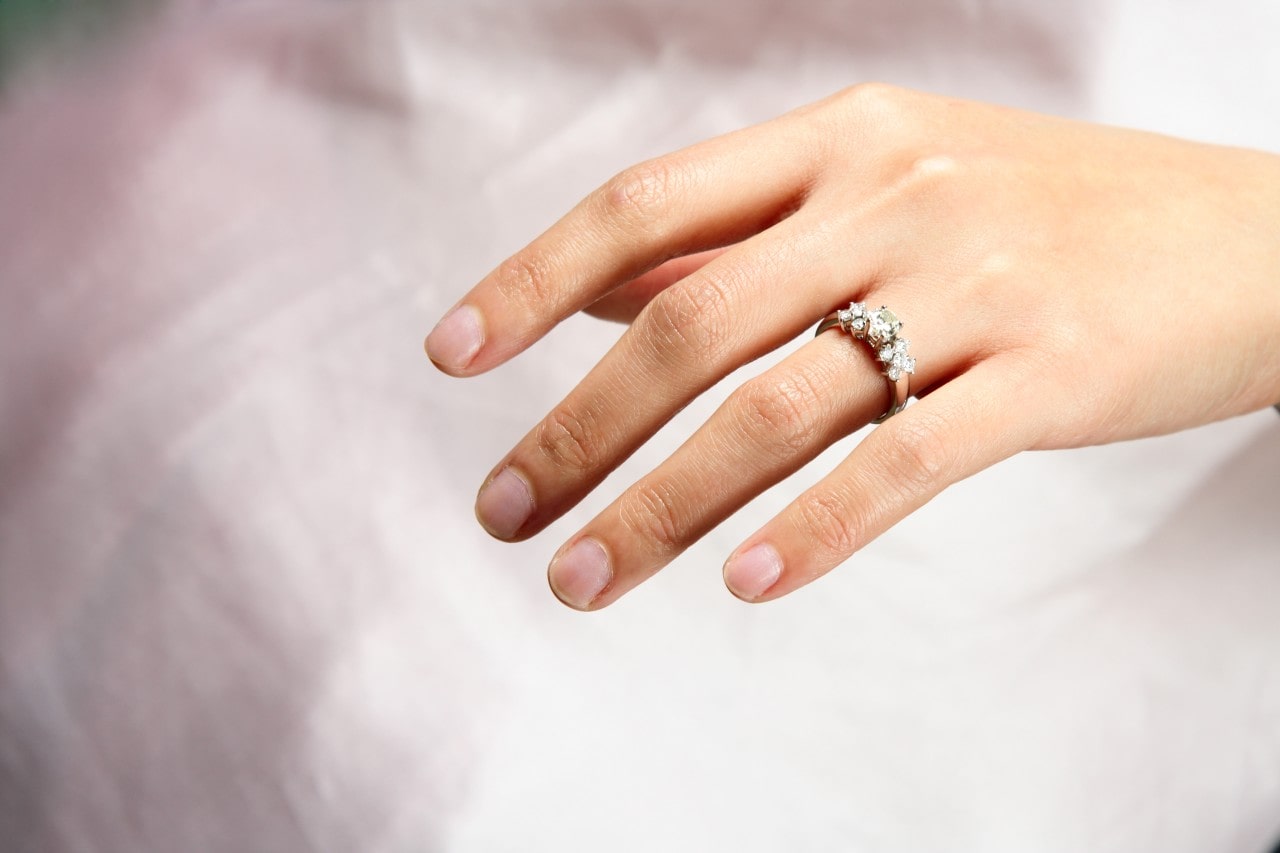 A hand with neatly trimmed nails rests gracefully on a soft white background, adorned with an elegant diamond ring.
