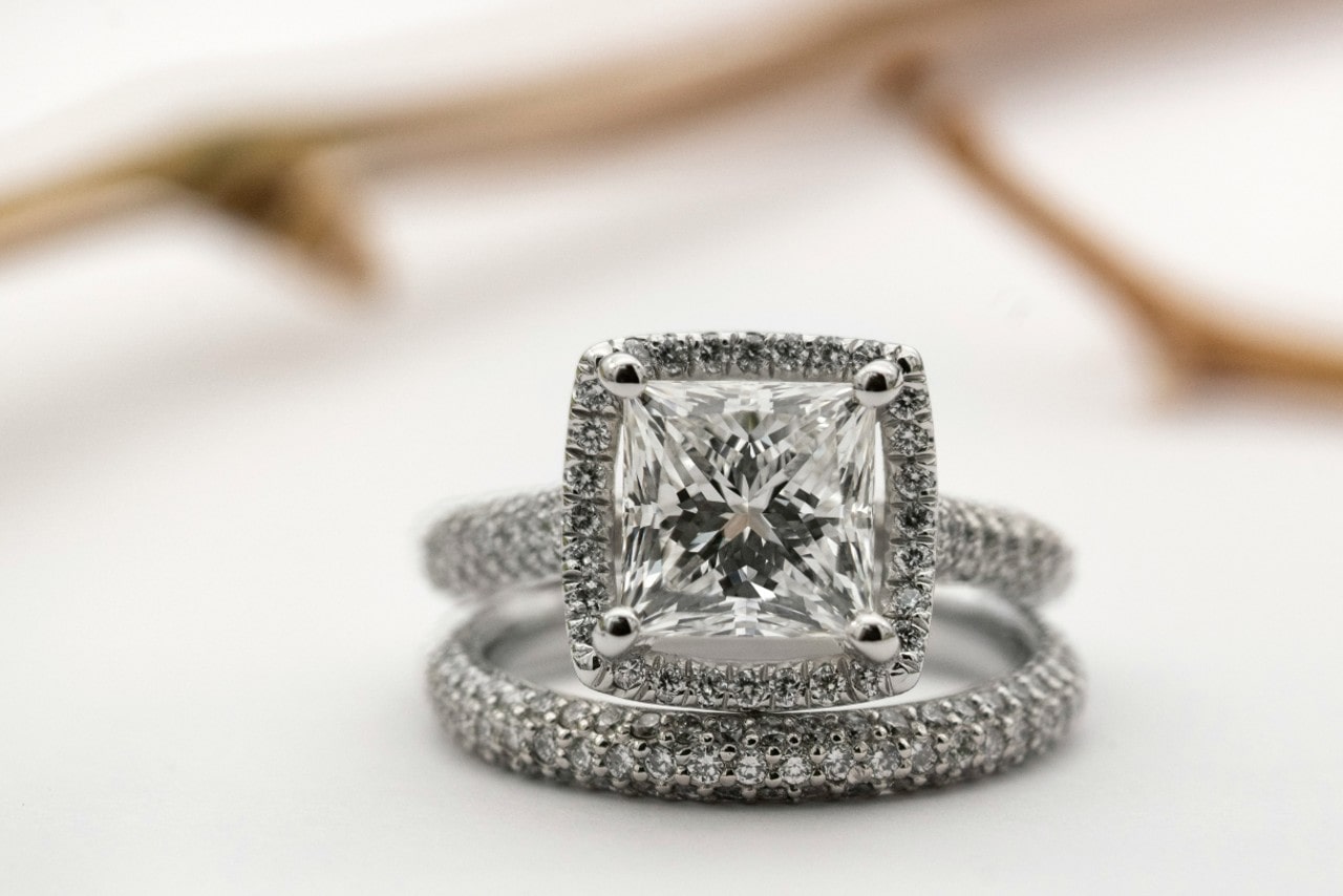 Sparkling square-cut diamond engagement ring with a halo setting paired with a diamond-encrusted wedding band on a soft, neutral background.