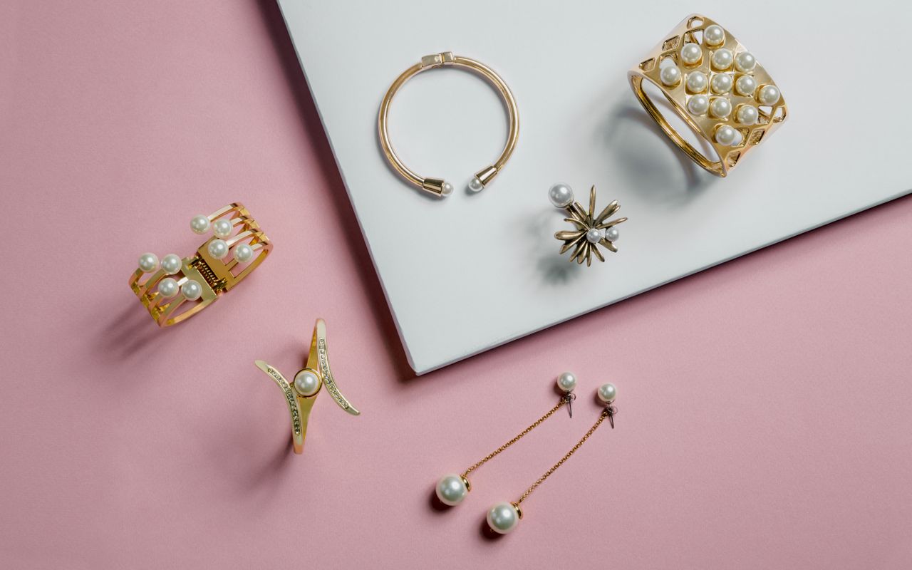 Assorted gold jewelry with pearls on a diagonal pink and white surface