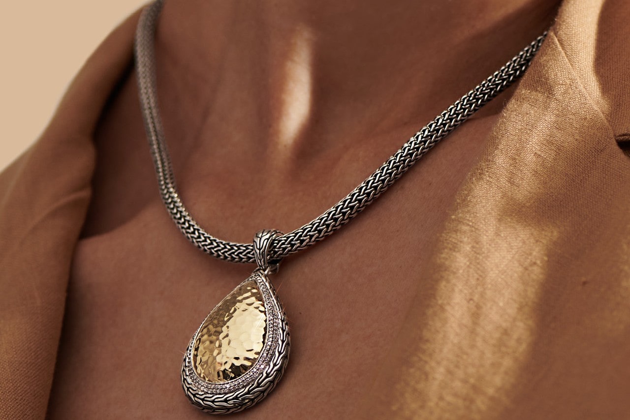 Close up image of a person’s neckline adorned with a silver and gold pendant necklace by John Hardy