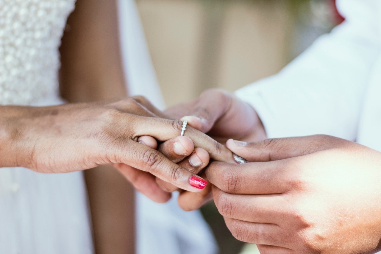 A man slips a diamond TACORI wedding band on his bride’s finger