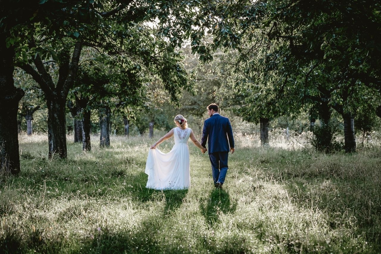 A newly wed couple walks through a field with trees