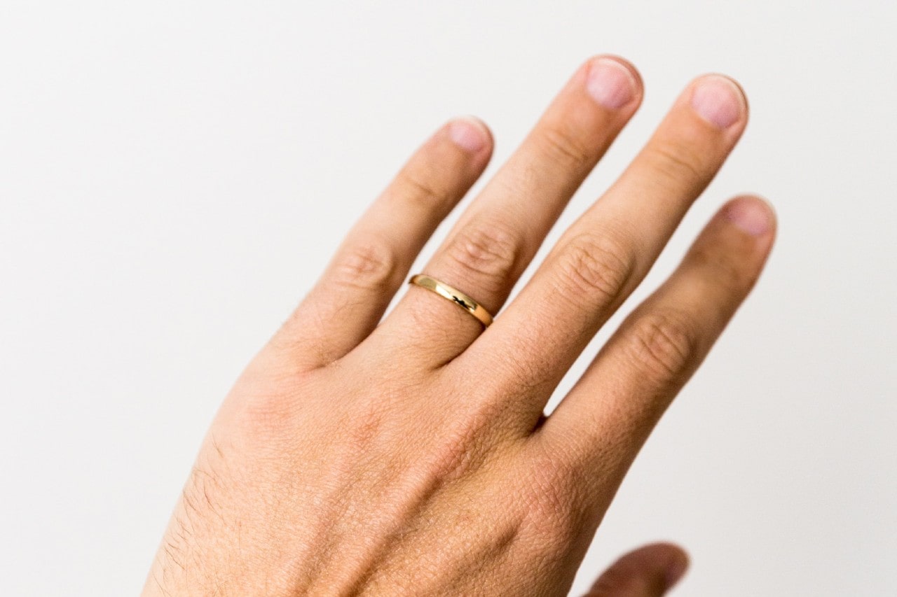 Close up image of a man’s hand wearing a simple, yellow gold wedding band