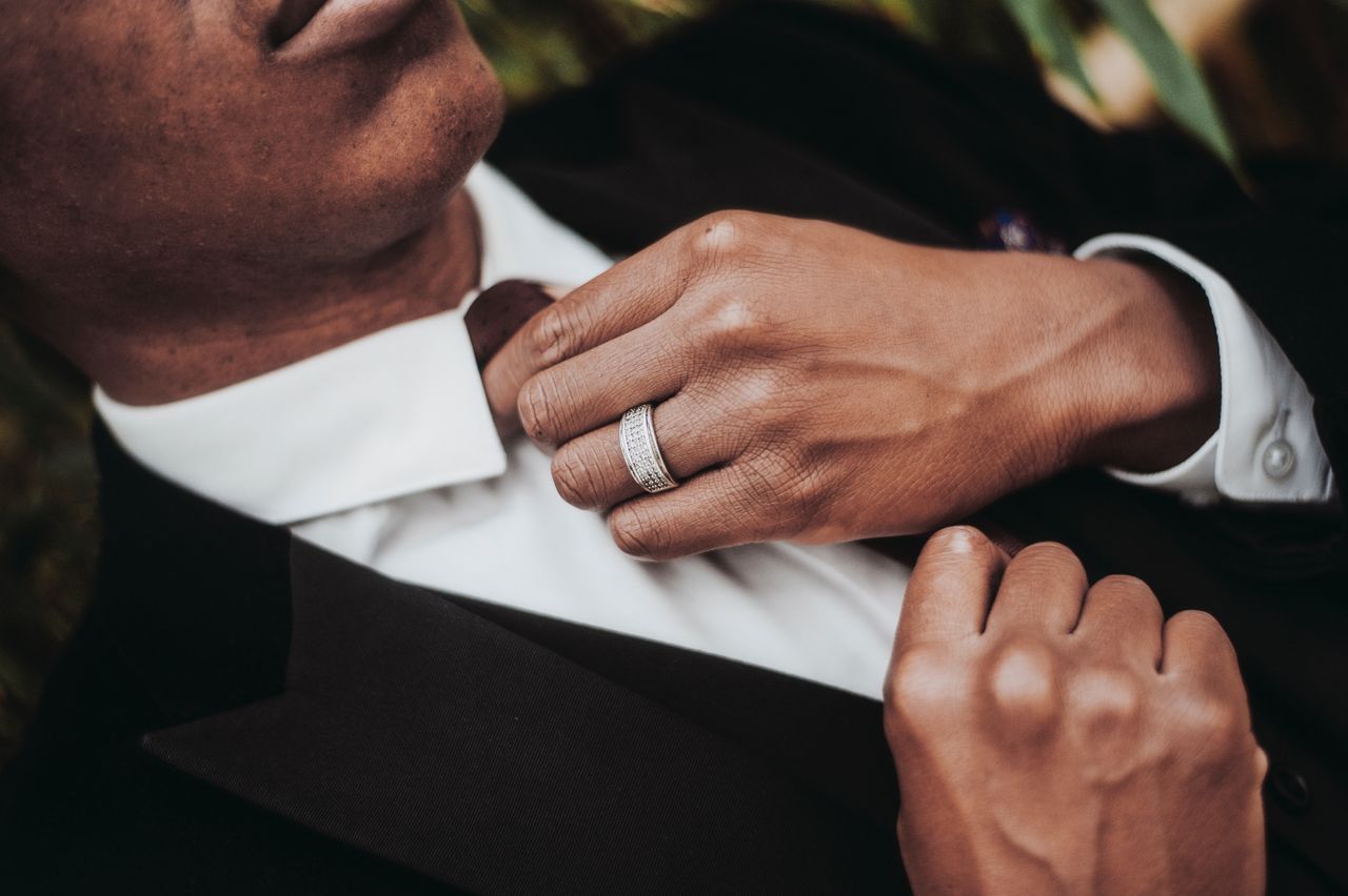 Close up image of a man adjusting his tie and wearing a white gold wedding band