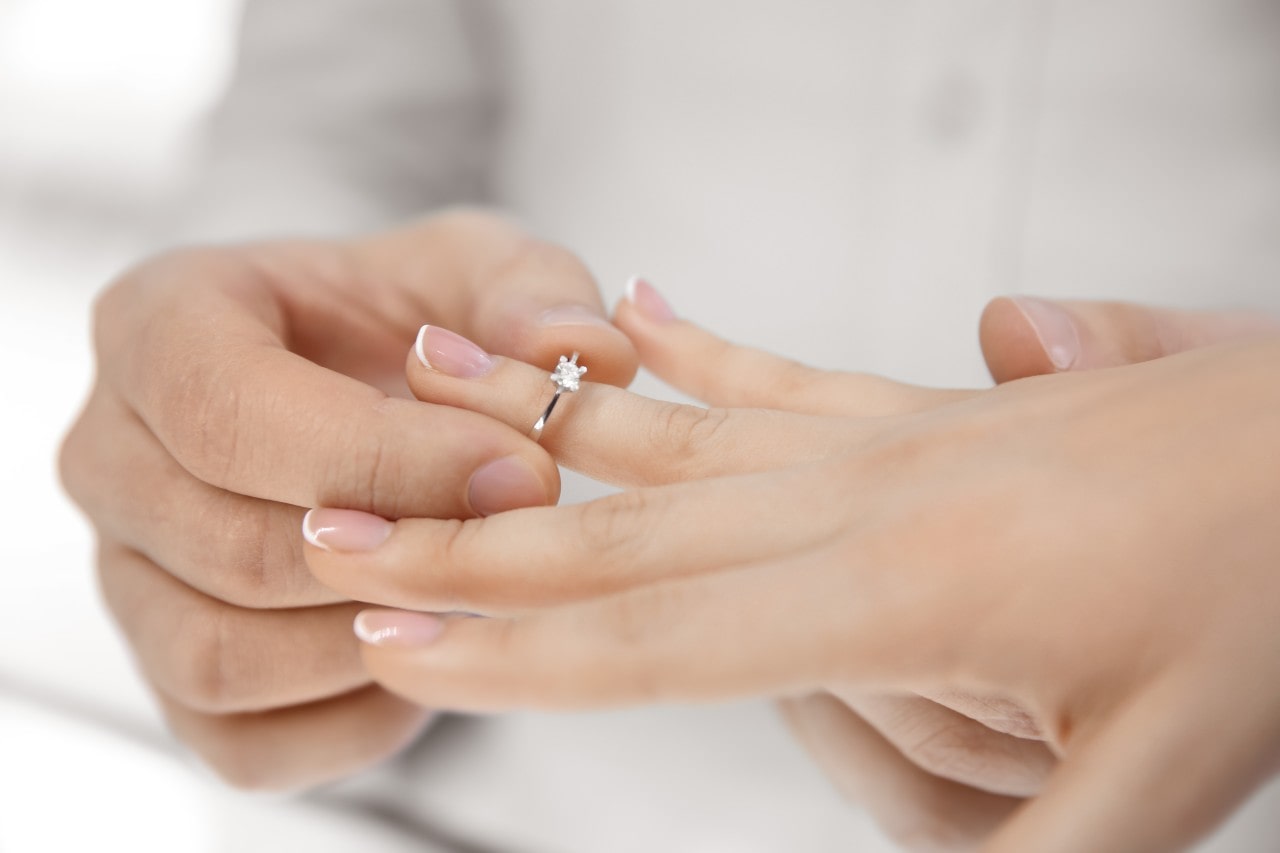 A man slips a princess cut diamond solitaire ring on a woman’s ring finger