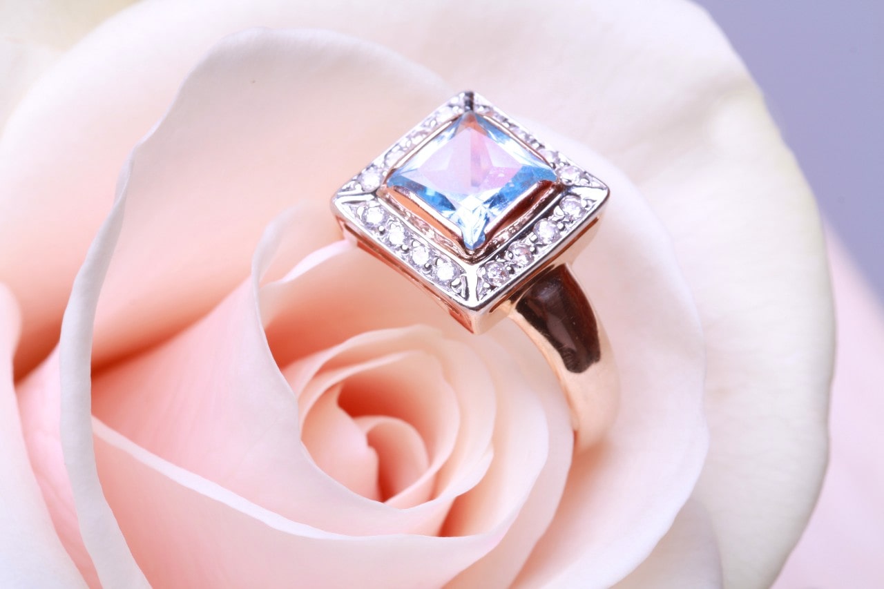 A rose-gold princess cut diamond ring sits in the petals of a pink rose