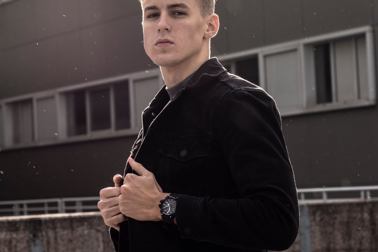 A man in a black coat wearing a black and white Aquaracer watch