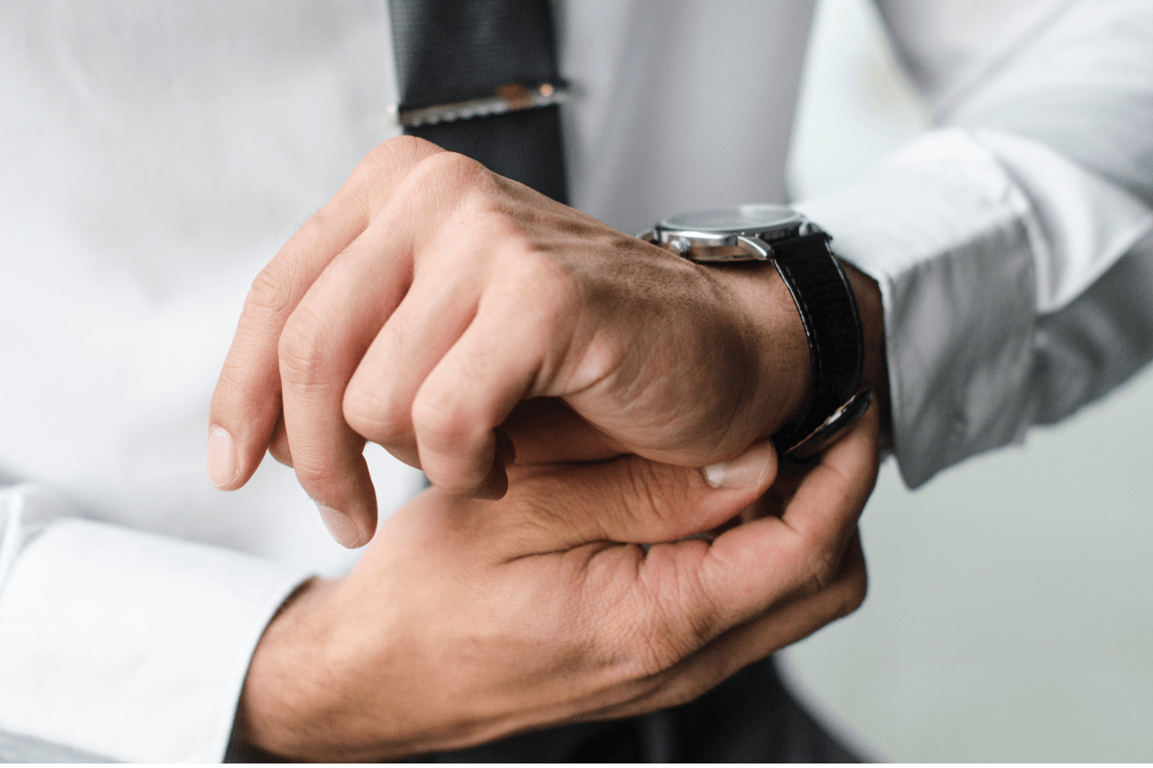 A close up of a man in a white shirt fixing his black leather wristwatch.