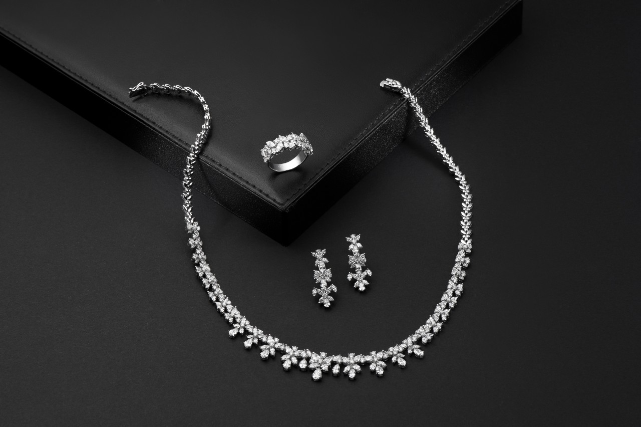An elegant jewelry set displayed on a black surface, featuring a sparkling diamond necklace, matching drop earrings, and a ring