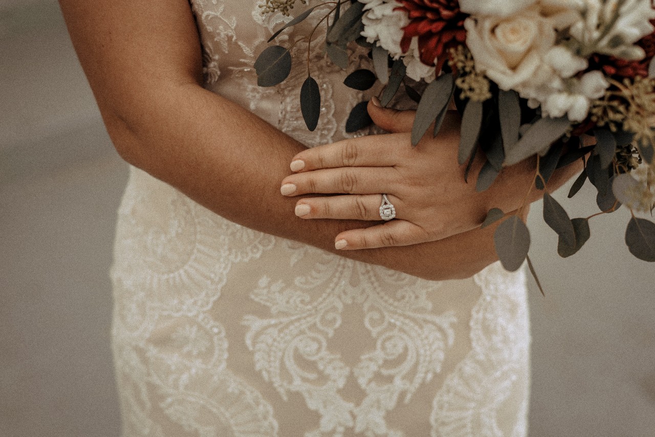 Split shank side stone details on this halo ring a bride is wearing is her beaded dress holding a bouquet of flowers