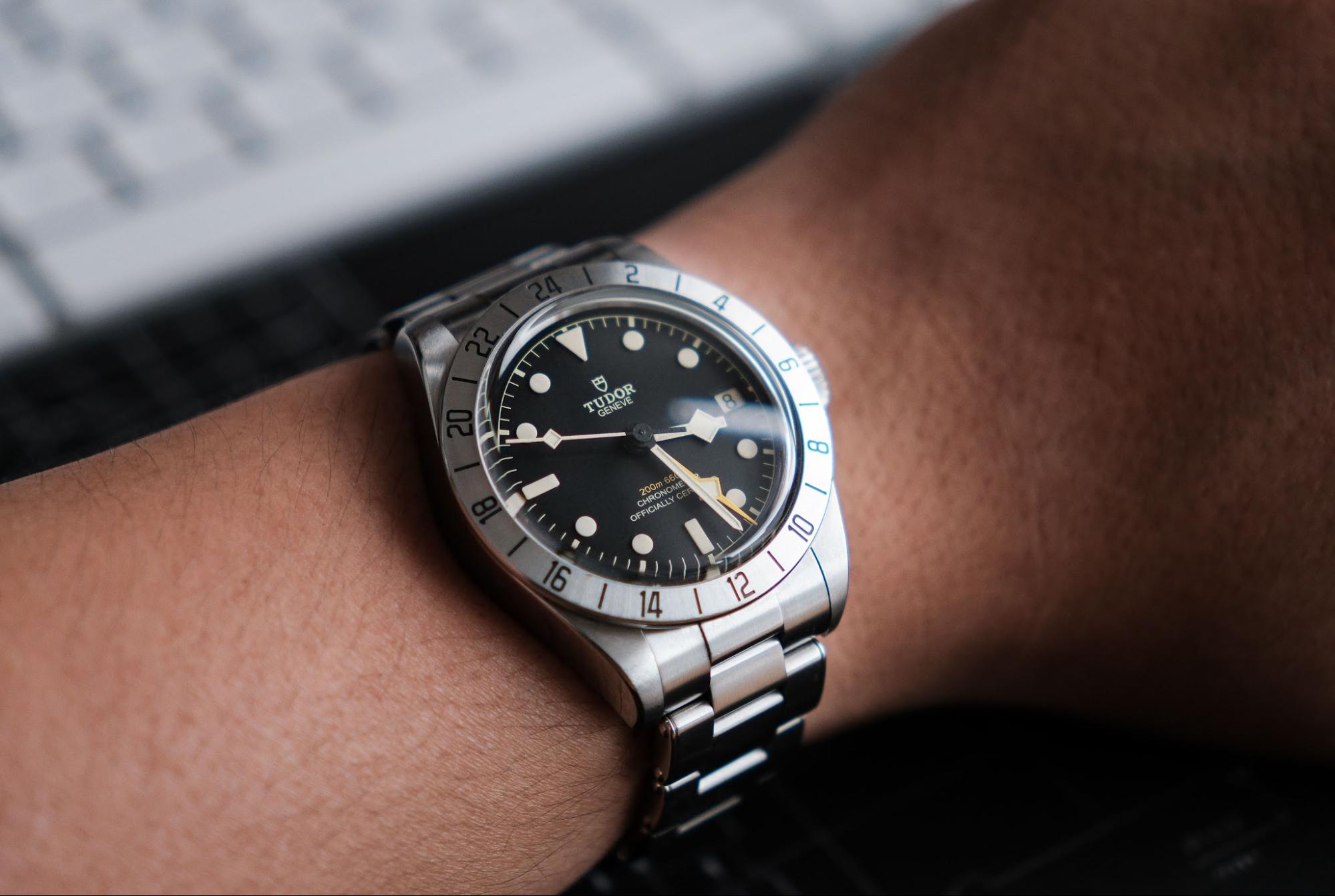 Close-up of a person wearing a stainless steel TUDOR Black Bay Pro GMT watch with a black dial and a fixed 24-hour bezel.