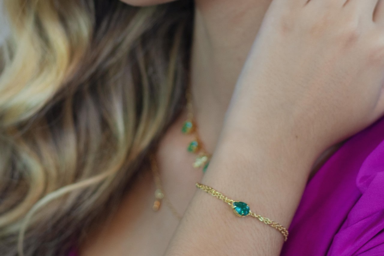 a woman wearing a yellow gold chain bracelet and a chain necklace with green gemstones