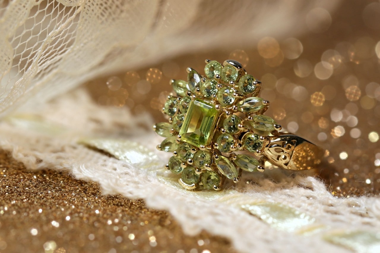 a yellow gold ring on a sparkling surface featuring many peridot stones in different cuts