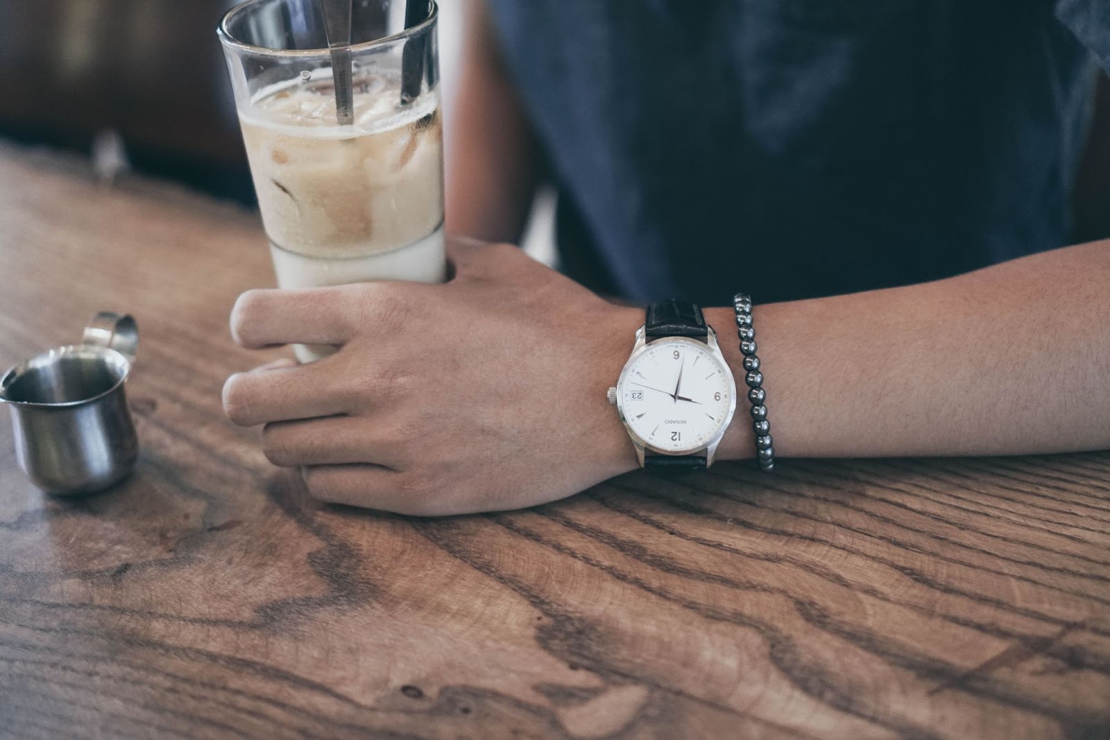 A man sips an iced coffee at a diner while wearing a minimal-style timepiece with a black alligator leather band