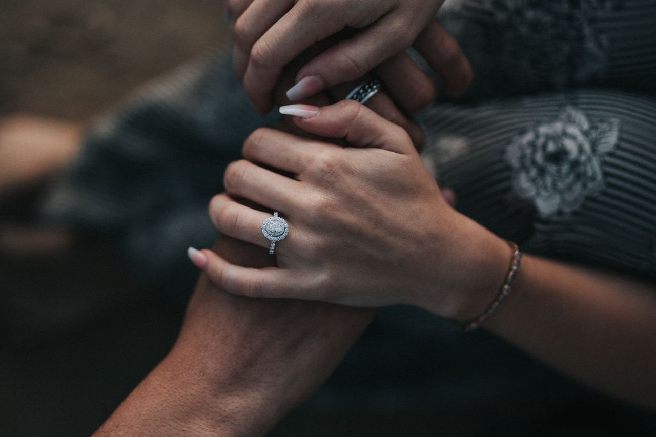 An oval halo engagement ring on the hand of a woman holding the hand of her love