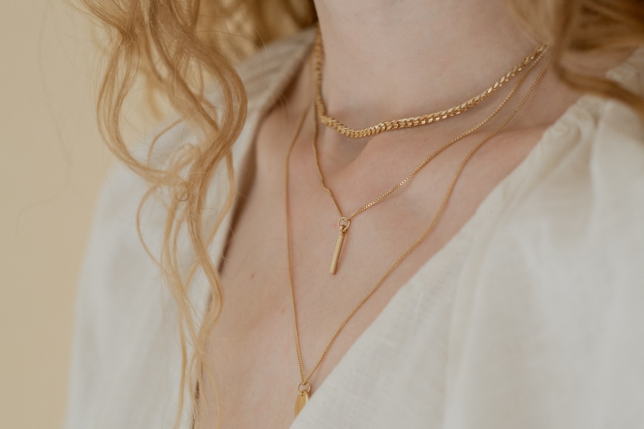 a trio of yellow gold necklaces of varying lengths adorn a woman’s neck.