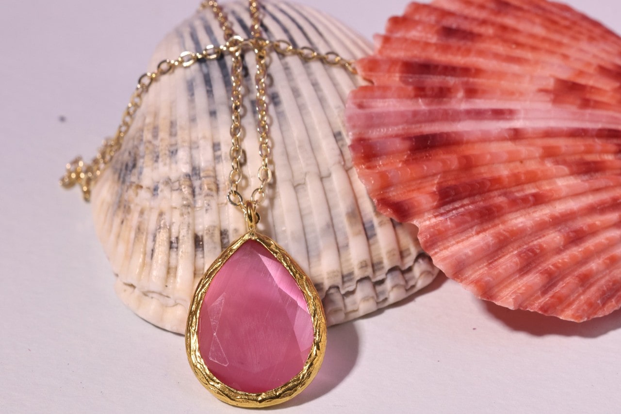 A pink gemstone necklace sits with two seashells.