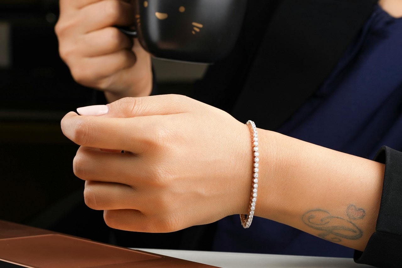 A close-up of a woman’s tattooed wrist, adorned with a subtle yet beautiful diamond tennis bracelet.