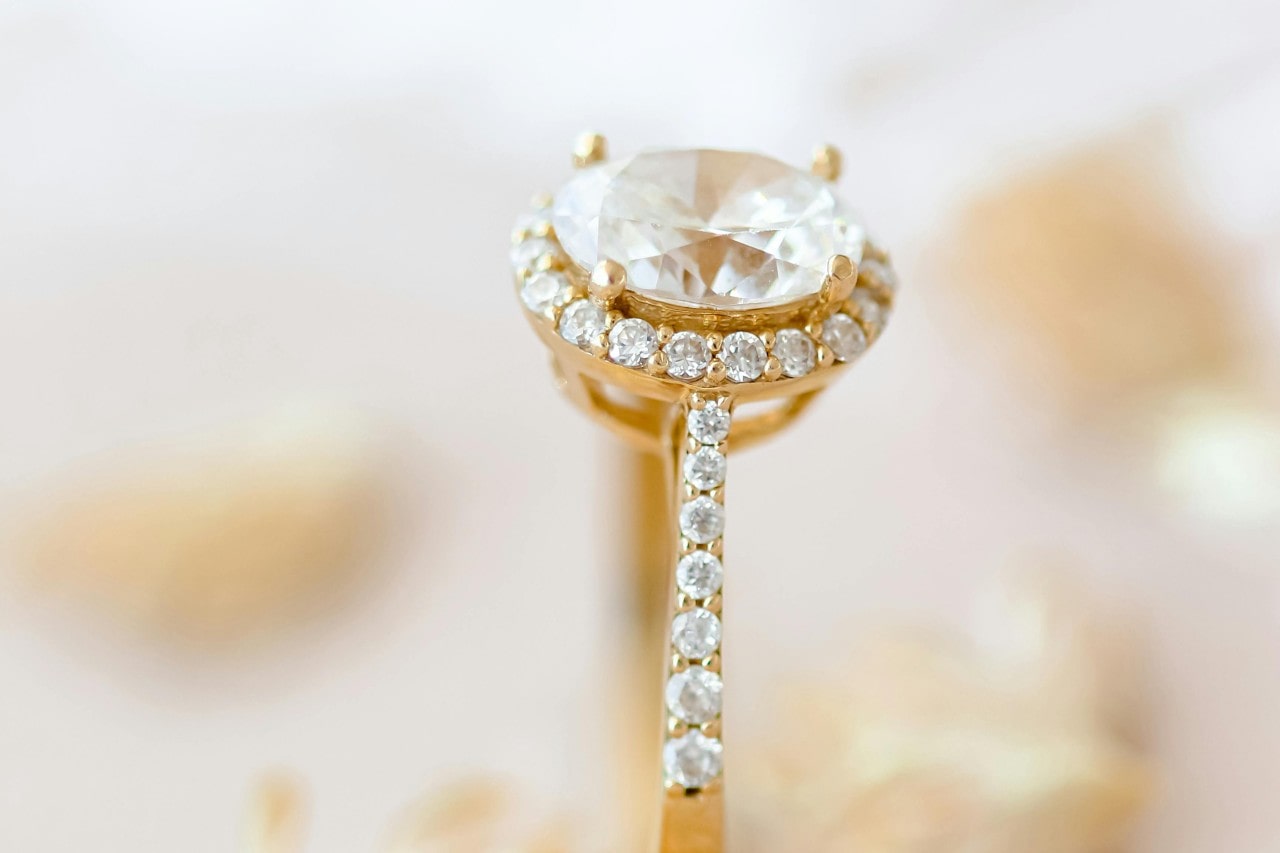 A close-up of a stunning diamond halo ring with glistening side stones on a bright background.