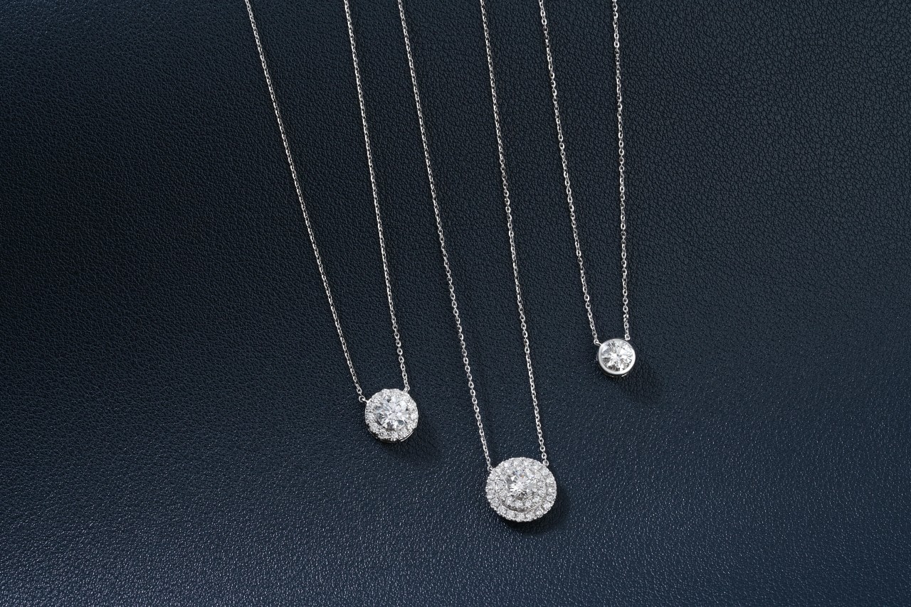 A close-up of three round diamond pendant necklaces on a textured black background.