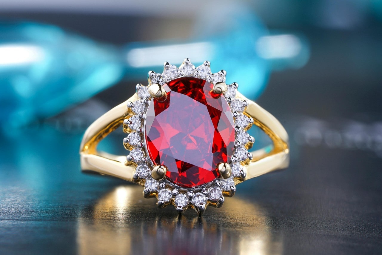 A close-up yellow gold ring with a ruby center stone and diamond halo.