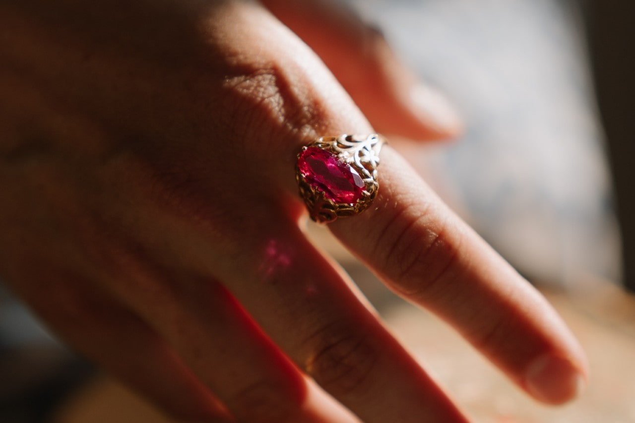 A woman’s hand wearing a red gemstone ring on her index finger.