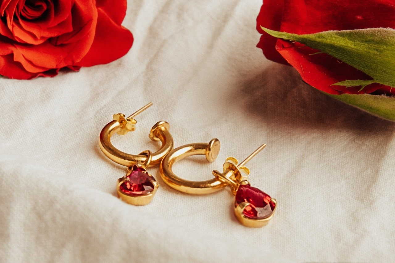 A pair of yellow gold earrings with red gemstones on a piece of beige fabric.