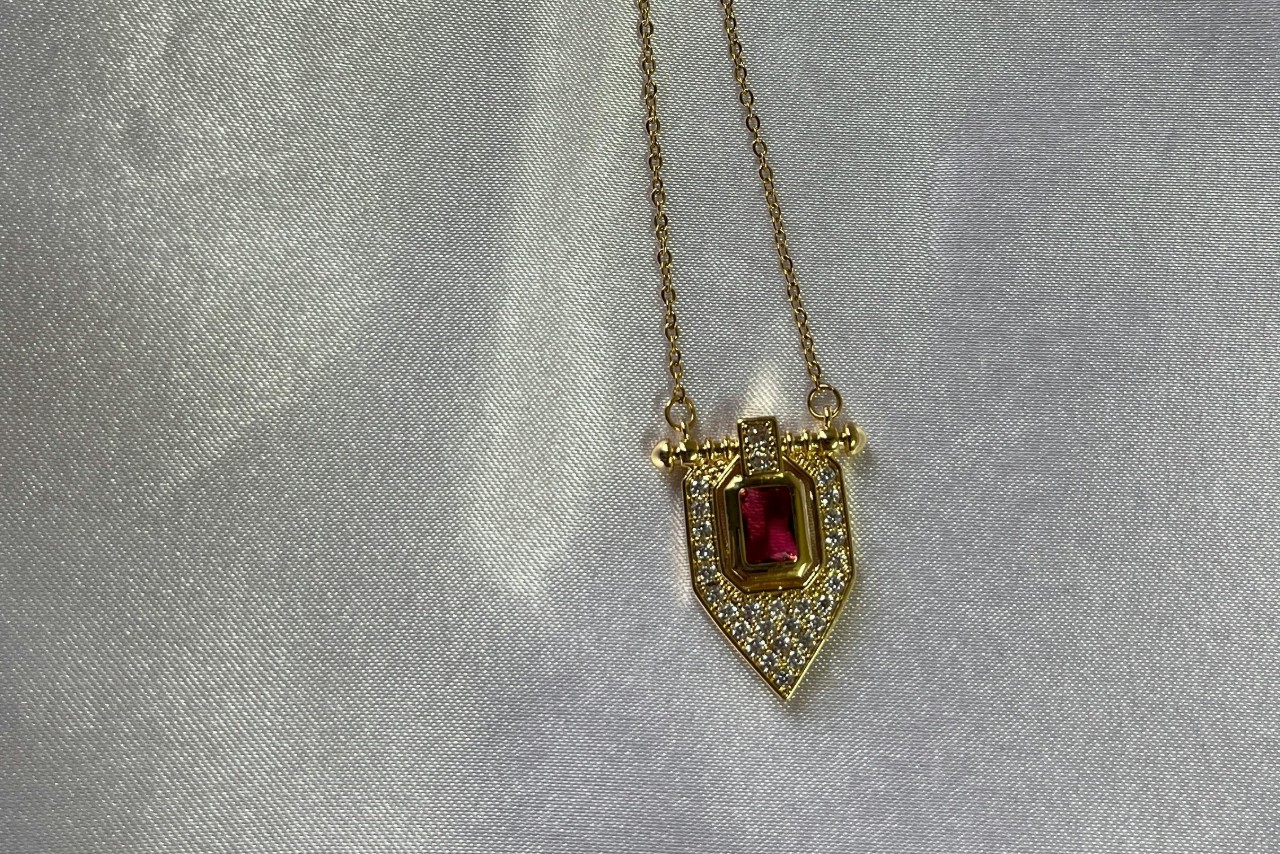 A yellow gold pendant necklace with a red center stone and diamond accents.