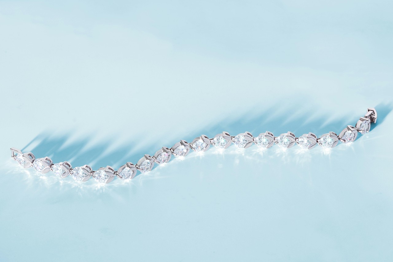 A top-down view of a glistening white gold tennis bracelet on a pale blue backdrop.