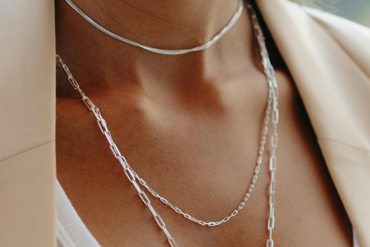 A close-up of a woman’s neck, adorned in gently layered white gold chain necklaces.